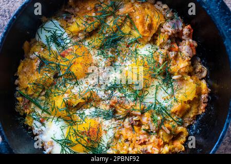 Riso bollito con uova fritte, zucca, peperoni, carote e cipolle in una padella di ghisa, primo piano. Cibo sfondo. Cibo sano Foto Stock