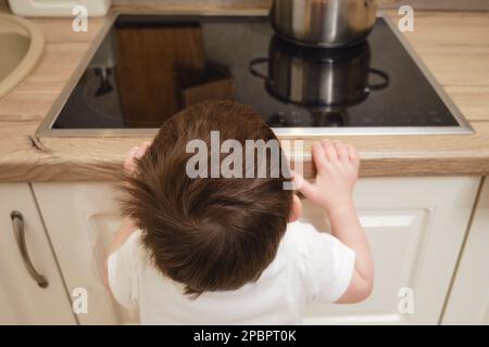 Il bambino salite su una stufa elettrica calda nella cucina domestica. Un bambino piccolo tocca la superficie della stufa con la mano al rischio di ottenere b Foto Stock