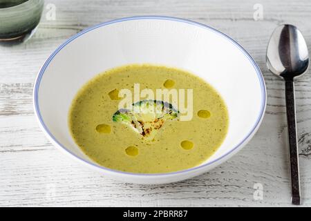 Sana zuppa di broccoli con una fetta di broccoli alla griglia su un piatto di porcellana bianca Foto Stock