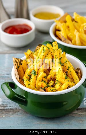 Fries francesi d'oro in una ciotola di smalto con salse varie sul lato Foto Stock