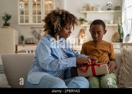 Emozionante regalo di apertura della madre afro-americana mentre festeggia la festa della mamma con il figlio a casa Foto Stock