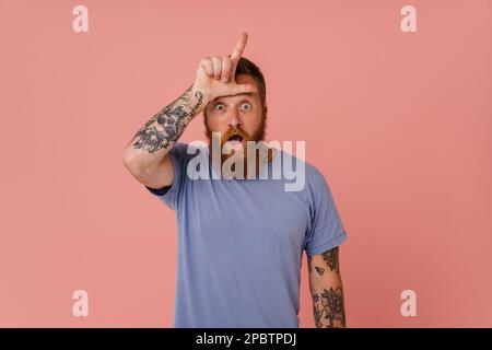 Lo zenzero scioccato con la barba che punta il dito verso l'alto isolato su sfondo rosa Foto Stock