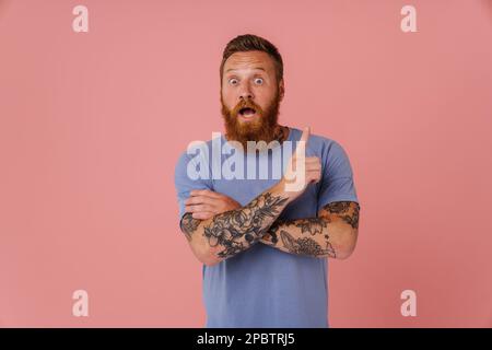 Lo zenzero scioccato con la barba che punta il dito verso l'alto isolato su sfondo rosa Foto Stock