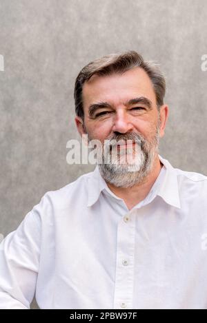 Ritratto di un uomo anziano seduto di fronte a uno sfondo grigio. Foto Stock