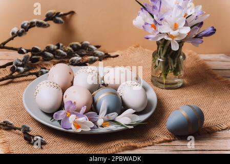 Piatto con uova di Pasqua dipinte, fiori primaverili e rami di salice su un tavolo di legno. Biglietto di auguri di Pasqua. Primo piano. Foto Stock