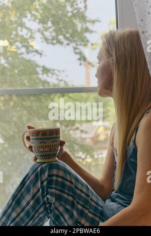 Donna di mezza età seduta in camera da letto gode mattina, bere caffè Foto Stock