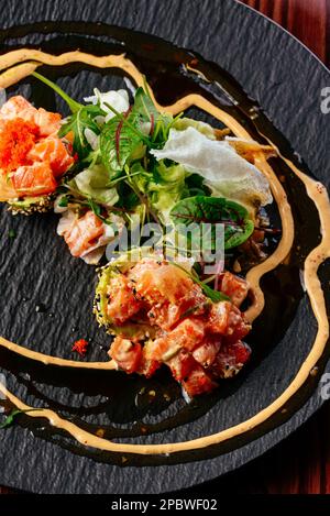 tartare di salmone con salsa ed erbe su un piatto nero Foto Stock