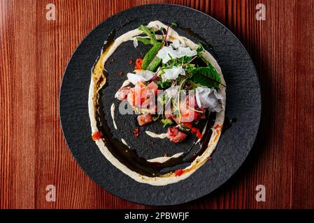 tartare di salmone con salsa ed erbe su un piatto nero Foto Stock
