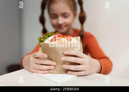 Bambina che mangia pita souvlaki nel ristorante greco. Capretto bianco di età elementare che tiene il panino grande gustoso in primo piano Foto Stock