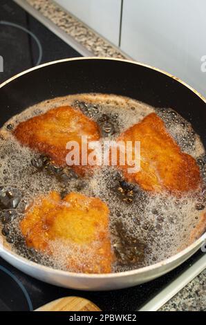 3 fette di Schnitzels impanate friggendo in olio caldo all'interno di una padella. Primo piano, vista dall'alto, nessuna persona. Foto Stock