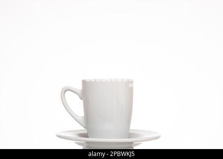 Small white ceramic coffee cup on a plate. Close up studio shot, isolated on white backgrou. Foto Stock