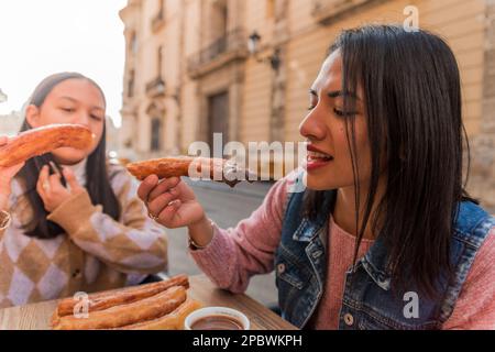 Particolare di una donna che mangia churro immerso nel cioccolato all'aperto. Foto Stock