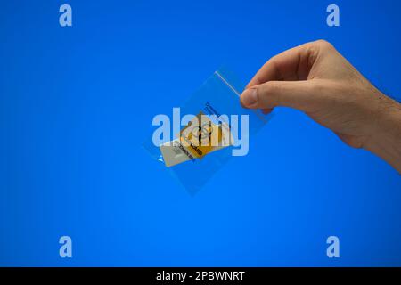 Piccolo sacchetto con chiusura a zip in plastica per lo smaltimento delle biowaste. Sacchetto per rifiuti per campioni a rischio biologico tenuto da un maschio caucasico a mano. Primo piano ripresa in studio, isolata sul backgrou blu Foto Stock