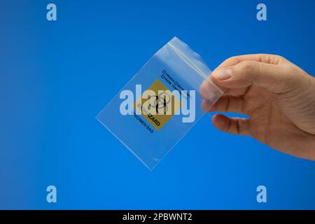 Piccolo sacchetto con chiusura a zip in plastica per lo smaltimento delle biowaste. Sacchetto per rifiuti per campioni a rischio biologico tenuto da un maschio caucasico a mano. Primo piano ripresa in studio, isolata sul backgrou blu Foto Stock