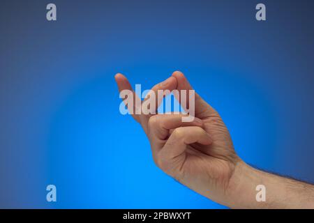 Gesto di scatto del dito da mano maschio caucasica. Primo piano ripresa in studio, isolata su sfondo blu. Foto Stock