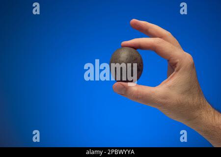 Maracuya cruda intera o frutti della passione tenuti in mano da maschio caucasico. Primo piano ripresa in studio, isolata su sfondo blu. Foto Stock