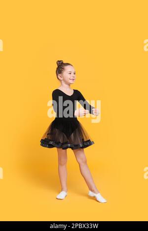Carina bambina in abito nero ballare su sfondo giallo Foto Stock