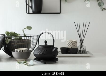 Elegante teiera nera e belle foglie di eucalipto verde sul tavolo bianco all'interno Foto Stock