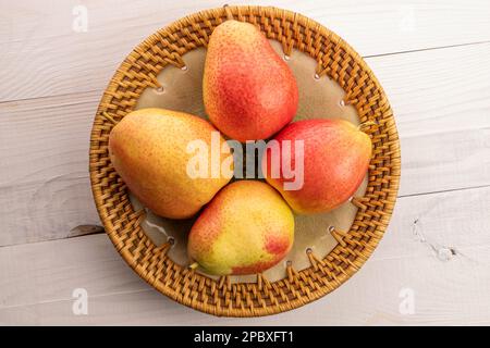 Quattro pere mature giallo-rosse in un piatto di ceramica su un tavolo di legno bianco. Foto Stock