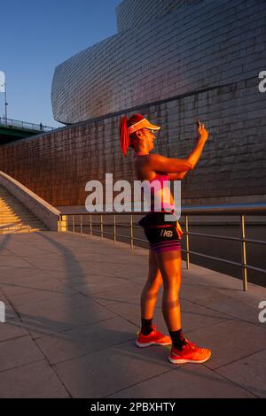 Bilbao, Spagna - 02 agosto 2022: Donna abbronzata in abbigliamento sportivo con corpo perfetto scatta foto selfie al telefono per i social media Foto Stock