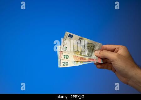 Una diffusione di banconote da 20, 10 e 5 euro, tenute in mano da un maschio caucasico. Primo piano ripresa in studio, isolata su sfondo blu. Foto Stock