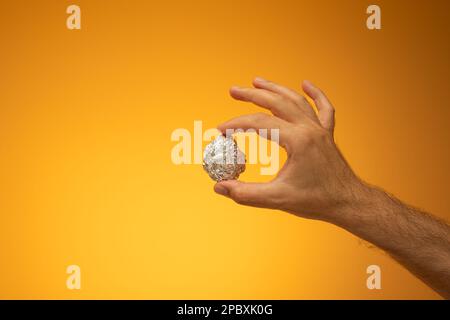 Foglio di teglia da cucina stropicciato in una palla tenuta in mano da mano maschio caucasica. Primo piano ripresa in studio, isolata su sfondo arancione. Foto Stock
