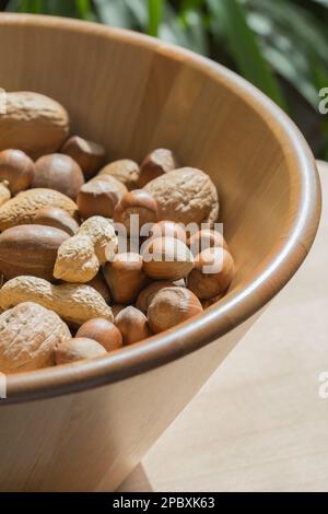 Vari tipi di noci assortiti in una grande ciotola di legno su uno sfondo verde verdeggiante. Fotografia macro Foto Stock