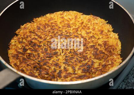 Rösti o rosti di patate fatti in casa in un'ampia padella su una stufa elettrica. Vista dall'alto, nessuna persona. Foto Stock