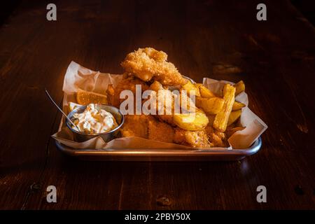 Piatto tradizionale inglese Pesce e patatine fritte serviti con patatine fritte su un tavolo di legno Foto Stock