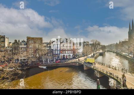 Incredibile vista del vecchio ponte che attraversa il canale tra gli edifici e gli alberi senza fronde sotto il cielo nuvoloso blu nel quartiere della città Foto Stock