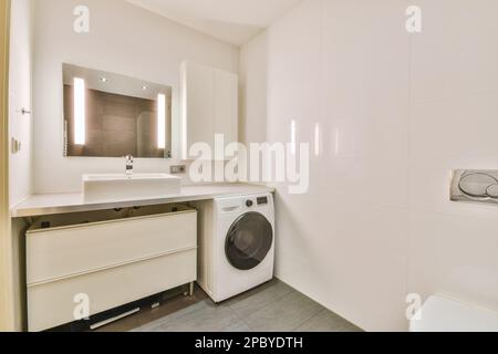 Elegante e moderno bagno bianco con lavatrice e lavabo collocato sul banco sotto lo specchio con illuminazione Foto Stock