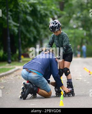 Rollerblading. L'allenatore corregge i movimenti del ragazzo insegnando lo slalom artistico. 25 giugno 2019. Kiev, Ucraina Foto Stock