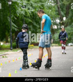 Rollerblading. L'allenatore corregge i movimenti del ragazzo insegnando lo slalom artistico. 25 giugno 2019. Kiev, Ucraina Foto Stock