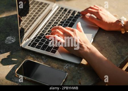 una bella donna matura in cappello lavora su un computer a un tavolo bianco in natura e trascorre la sua giornata in modo produttivo Foto Stock