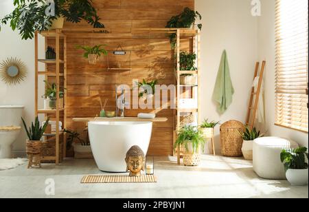 Elegante bagno interno con vasca bianca e piante verdi vicino alle pareti in legno. Idea per il design Foto Stock