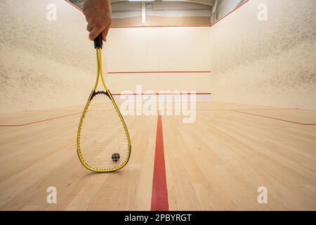 Mano maschile che tiene una racchetta all'interno di un campo da squash. Angolo basso, persona non riconoscibile, grande profondità di campo Foto Stock