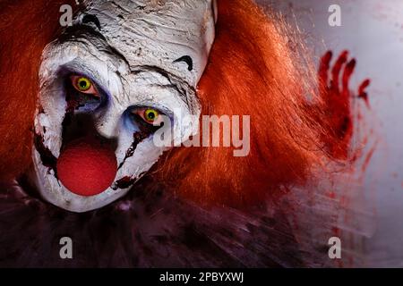 Clown terrificante contro pellicola di plastica macchiata di sangue, primo piano. Costume da festa di Halloween Foto Stock