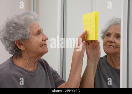 Donna anziana che guarda la nota di promemoria al chiuso. Compromissione della memoria correlata all'età Foto Stock