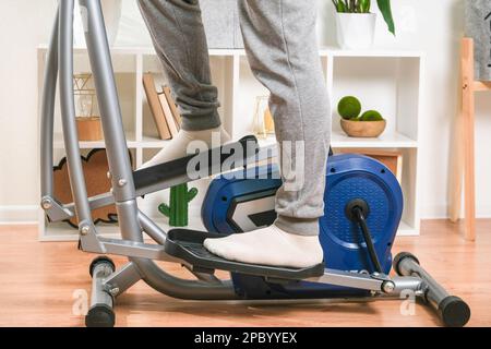 Un uomo si allena su una macchina ellittica. Allenatore sportivo a casa in appartamento. Sport a casa. Foto Stock