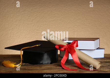 Cappello di laurea, libri e diploma su tavola di legno Foto Stock