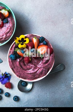 Due ciotole estive di acai frullato con fragole, mirtilli, su fondo grigio in cemento. Ciotola per la colazione con frutta e cereali, primo piano, vista dall'alto Foto Stock