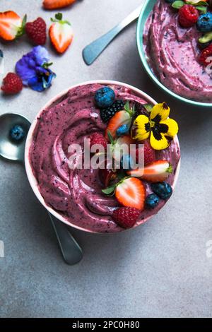 Due ciotole estive di acai frullato con fragole, mirtilli, su fondo grigio in cemento. Ciotola per la colazione con frutta e cereali, primo piano, vista dall'alto Foto Stock