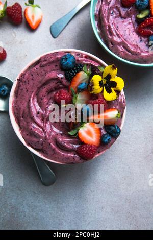 Due ciotole estive di acai frullato con fragole, mirtilli, su fondo grigio in cemento. Ciotola per la colazione con frutta e cereali, primo piano, vista dall'alto Foto Stock