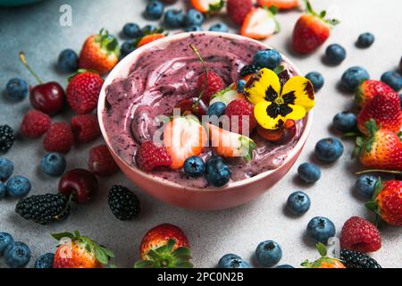 Due ciotole estive di acai frullato con fragole, mirtilli, su fondo grigio in cemento. Ciotola per la colazione con frutta e cereali, primo piano, vista dall'alto Foto Stock