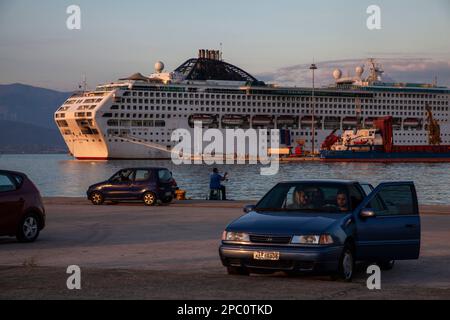 Un porto sulla spiaggia con una varietà di auto e una grande nave da crociera ormeggiata in primo piano Foto Stock