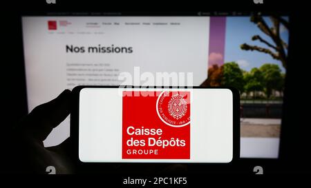 Persona che tiene in mano uno smartphone con il logo di Caisse des Depots et Consignations (CDC) sullo schermo davanti al sito Web. Messa a fuoco sul display del telefono. Foto Stock