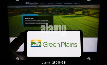 Persona in possesso di smartphone con il logo della società di etanolo US Green Plains Inc. Sullo schermo di fronte al sito Web. Messa a fuoco sul display del telefono. Foto Stock