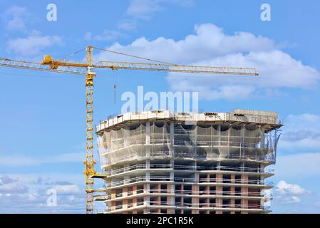 Gru a torre sullo sfondo della costruzione di un alto edificio residenziale a più piani contro un cielo nuvoloso blu. Spazio di copia. Foto Stock