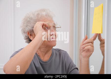 Donna anziana che guarda la nota di promemoria al chiuso. Compromissione della memoria correlata all'età Foto Stock