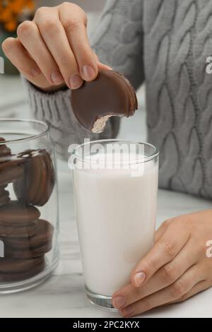 Donna che immerga deliziosa torta di cioccolato in un bicchiere di latte a tavola di marmo bianco, primo piano Foto Stock